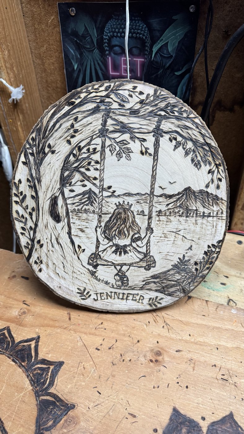 Little Princess — finished woodburning of a girl in a crown on a tree swing by a mountain lake, named Jennifer